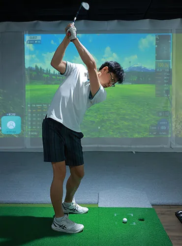 Man in mid-swing on an indoor golf simulator.